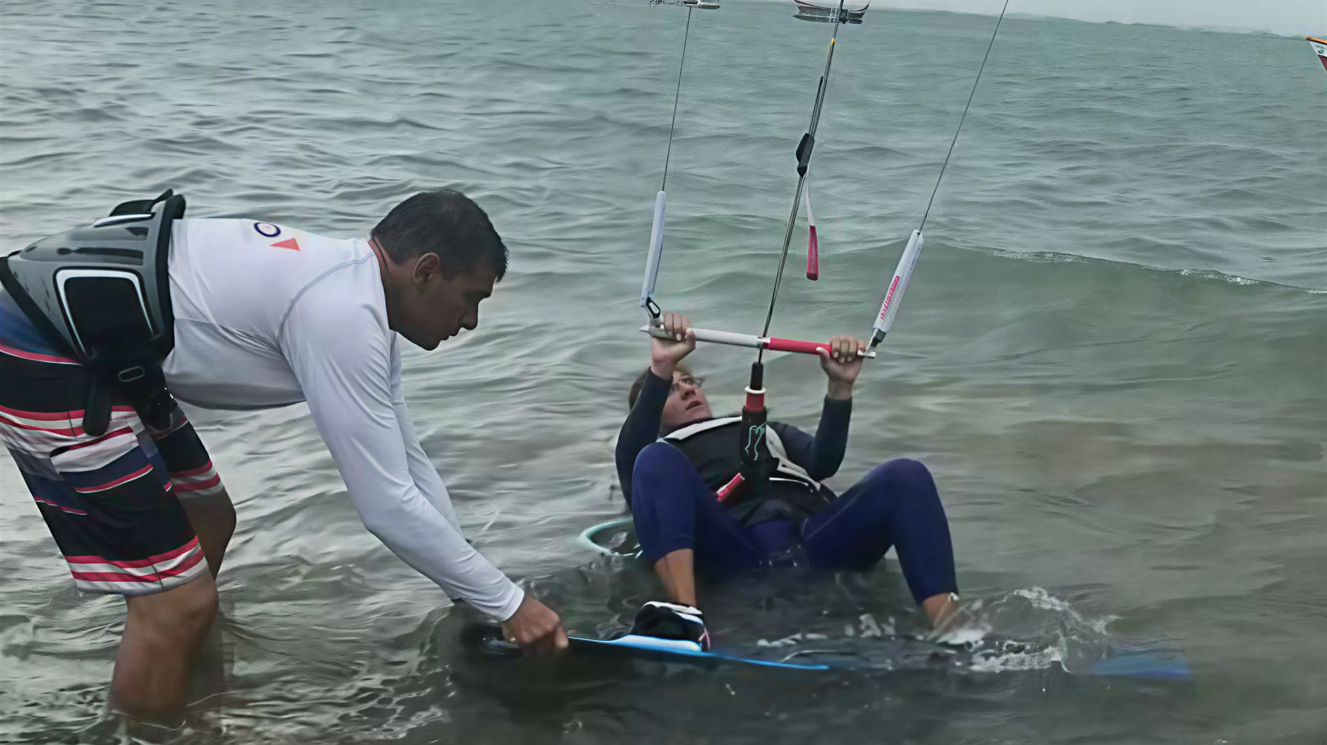 Tabla y cometa sobre el agua, la orilla al fondo.